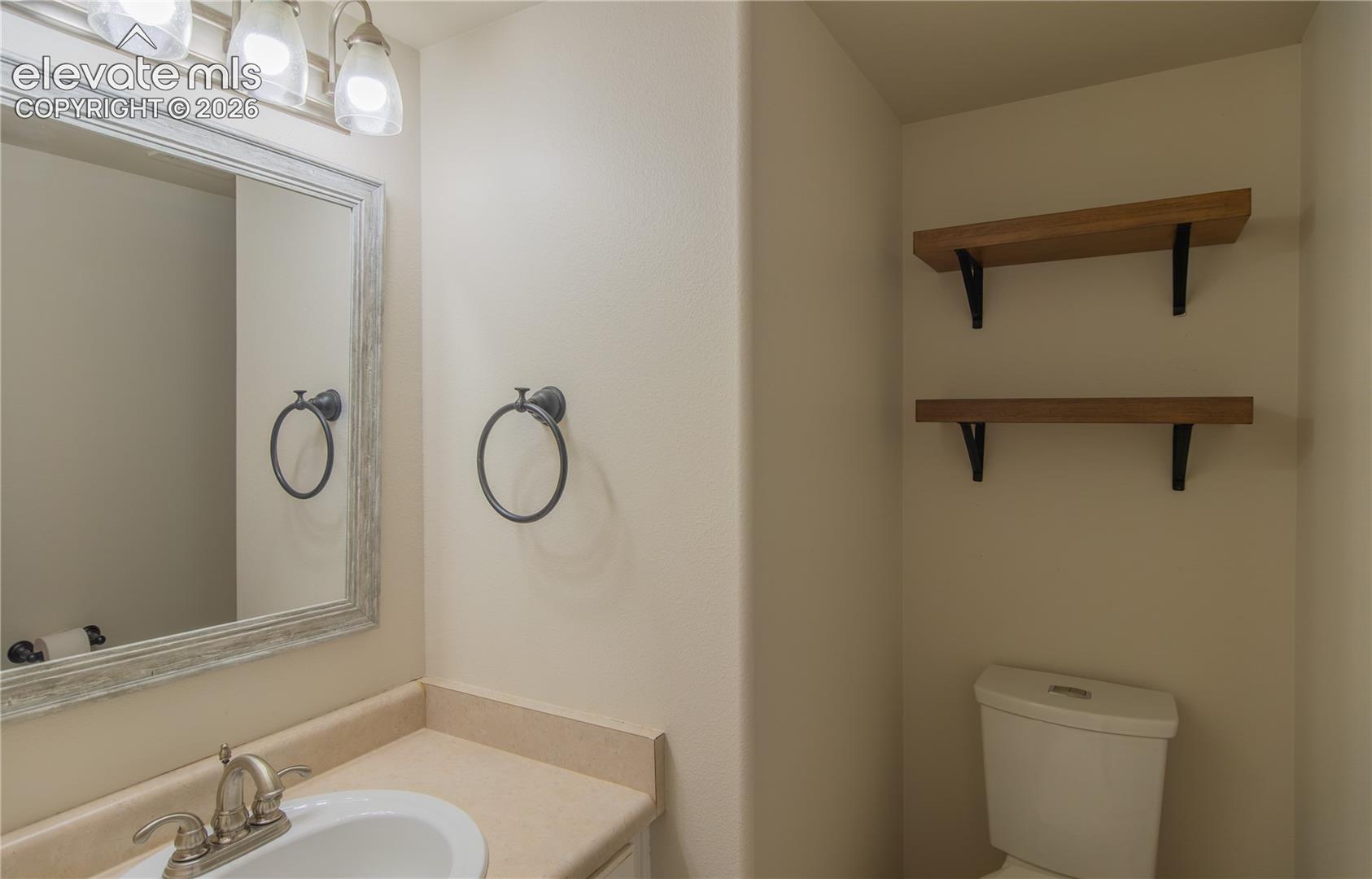 Convenient powder room with a decorative framed mirror, updated lighting, and floating shelves.