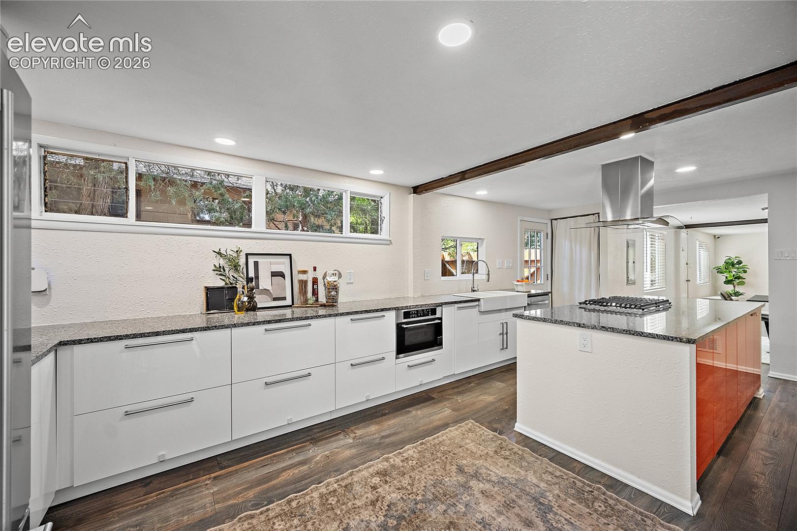 Modern kitchen featuring white flat-panel cabinetry, granite countertops, a built-in oven, a stainless steel range hood, and wood-finish flooring
