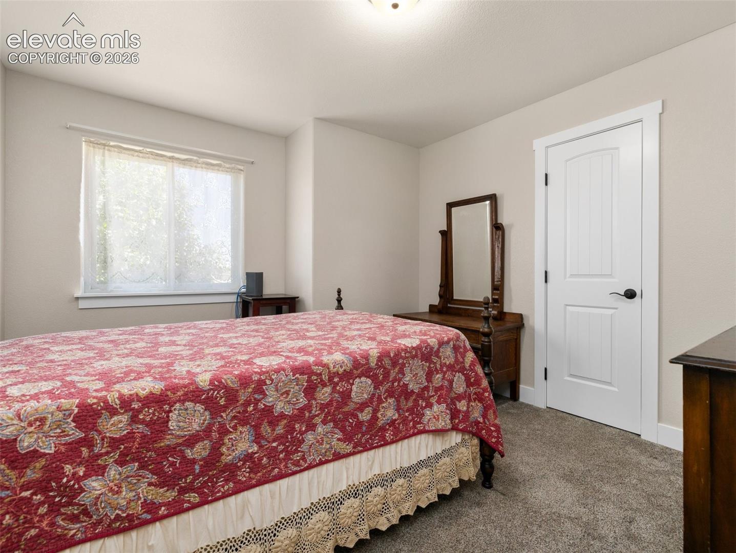 Carpeted flooring, white trim, natural light from a window, and a white interior door with black hardware