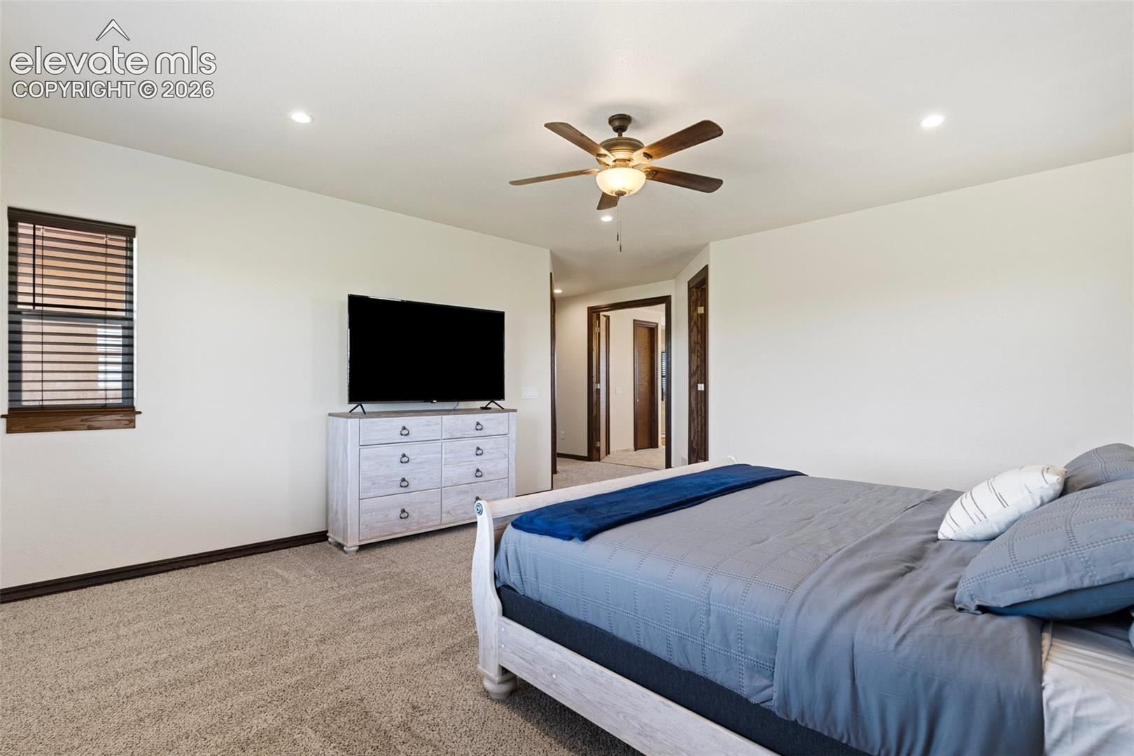 Carpeted primary bedroom featuring recessed lighting, a ceiling fan with light fixture, and a window with wood blinds