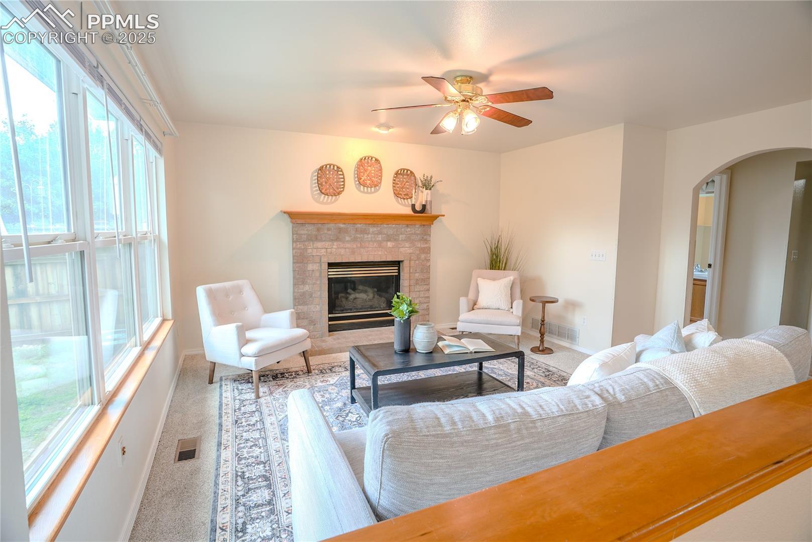 Living room with carpet floors, arched walkways, a fireplace, and a ceiling fan