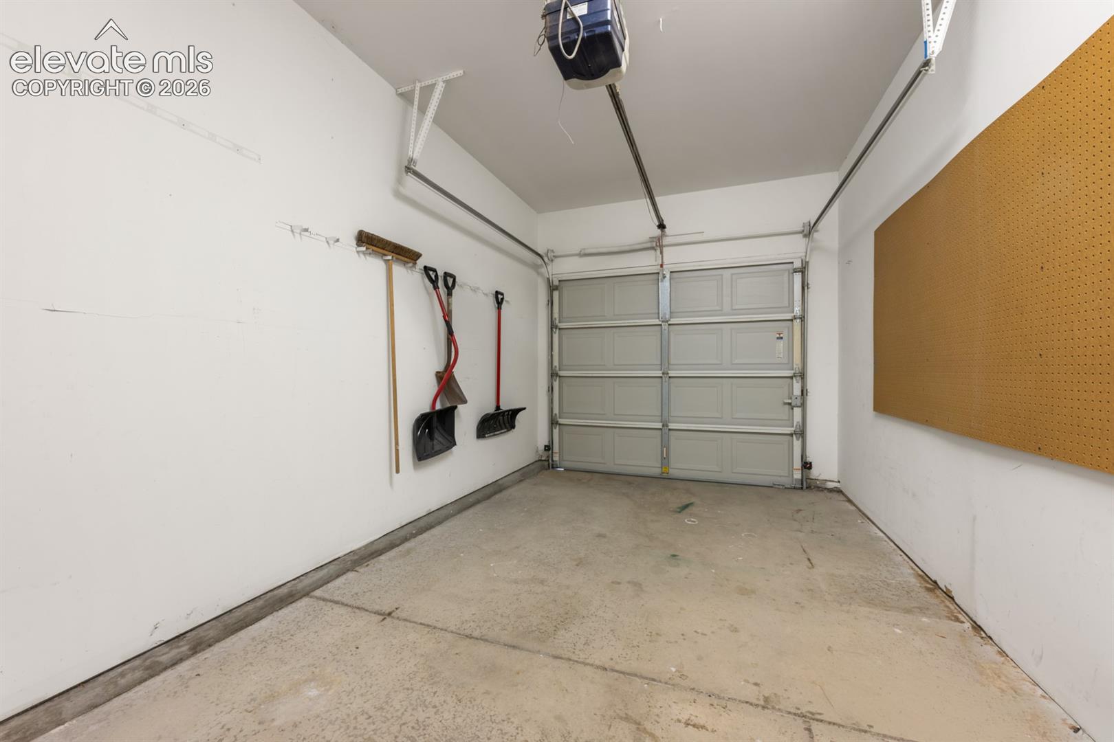 Garage space featuring a concrete floor, sectional overhead door, automated door opener, and a wall-mounted pegboard