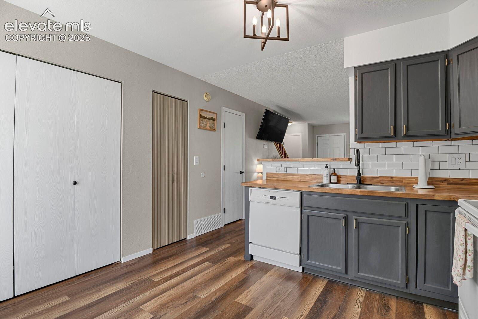 Kitchen featuring dark gray cabinetry, wood-finish countertops, subway tile backsplash, and a stainless steel sink with a matte black faucet