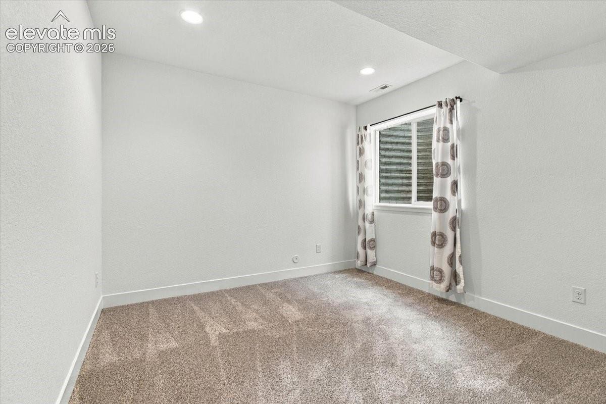 Neutral interior space featuring wall-to-wall carpeting, recessed ceiling lighting, and a window with a corrugated metal egress well