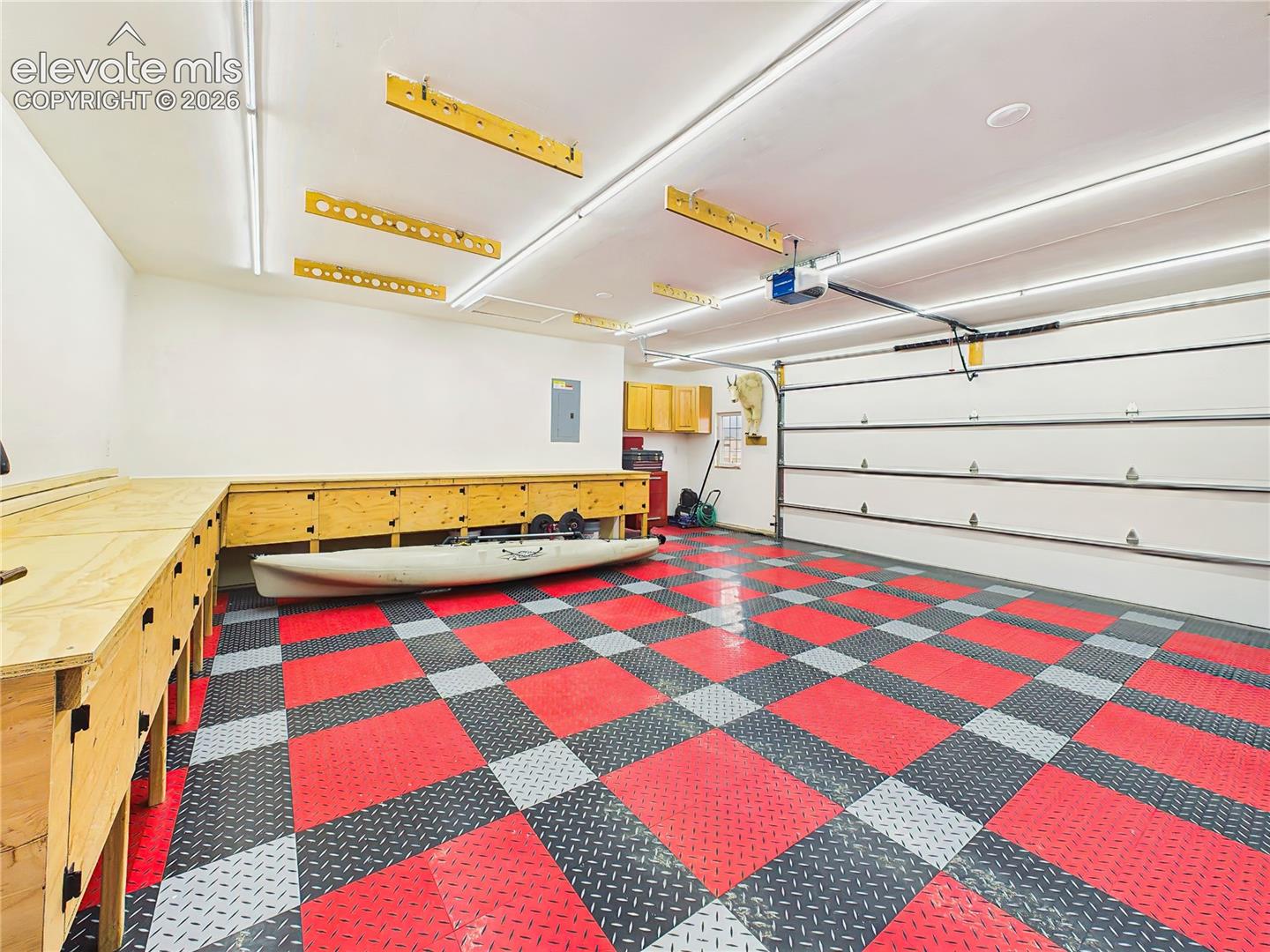 Oversized garage is thoughtfully outfitted with custom built-in workbenches, bright overhead lighting, and durable modular flooring, creating an ideal space for projects, storage, or hobbies.