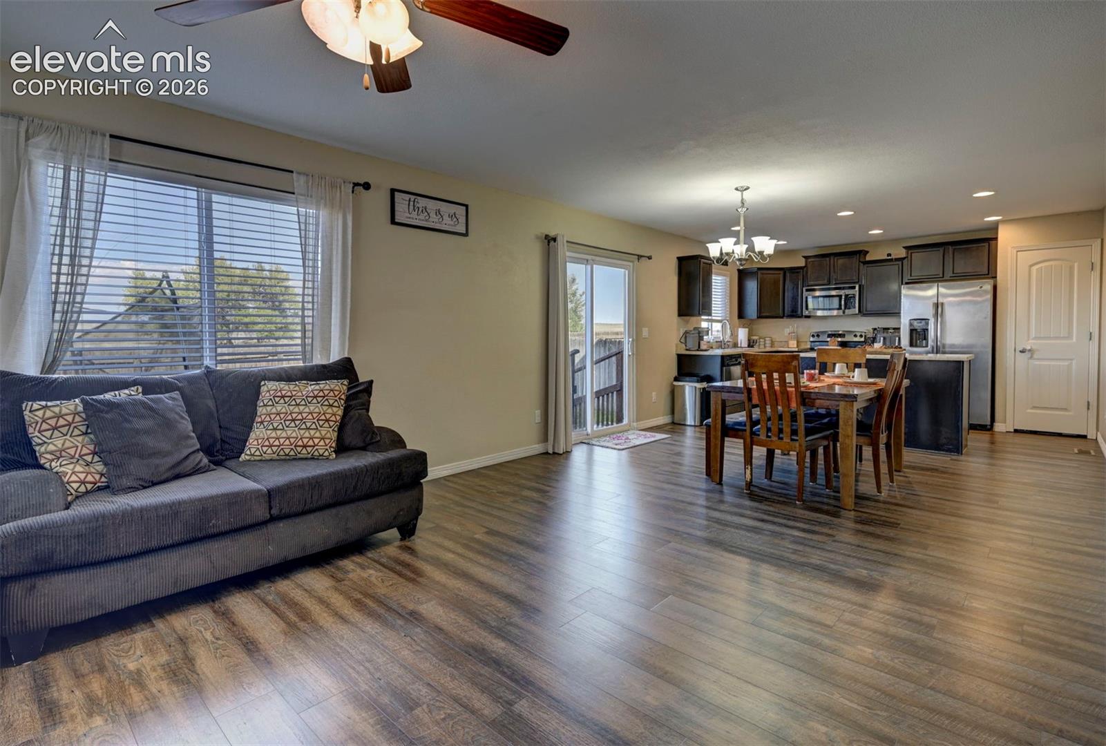 Open-concept living area with wood-finish flooring, a ceiling fan with integrated lighting, and a window with blinds