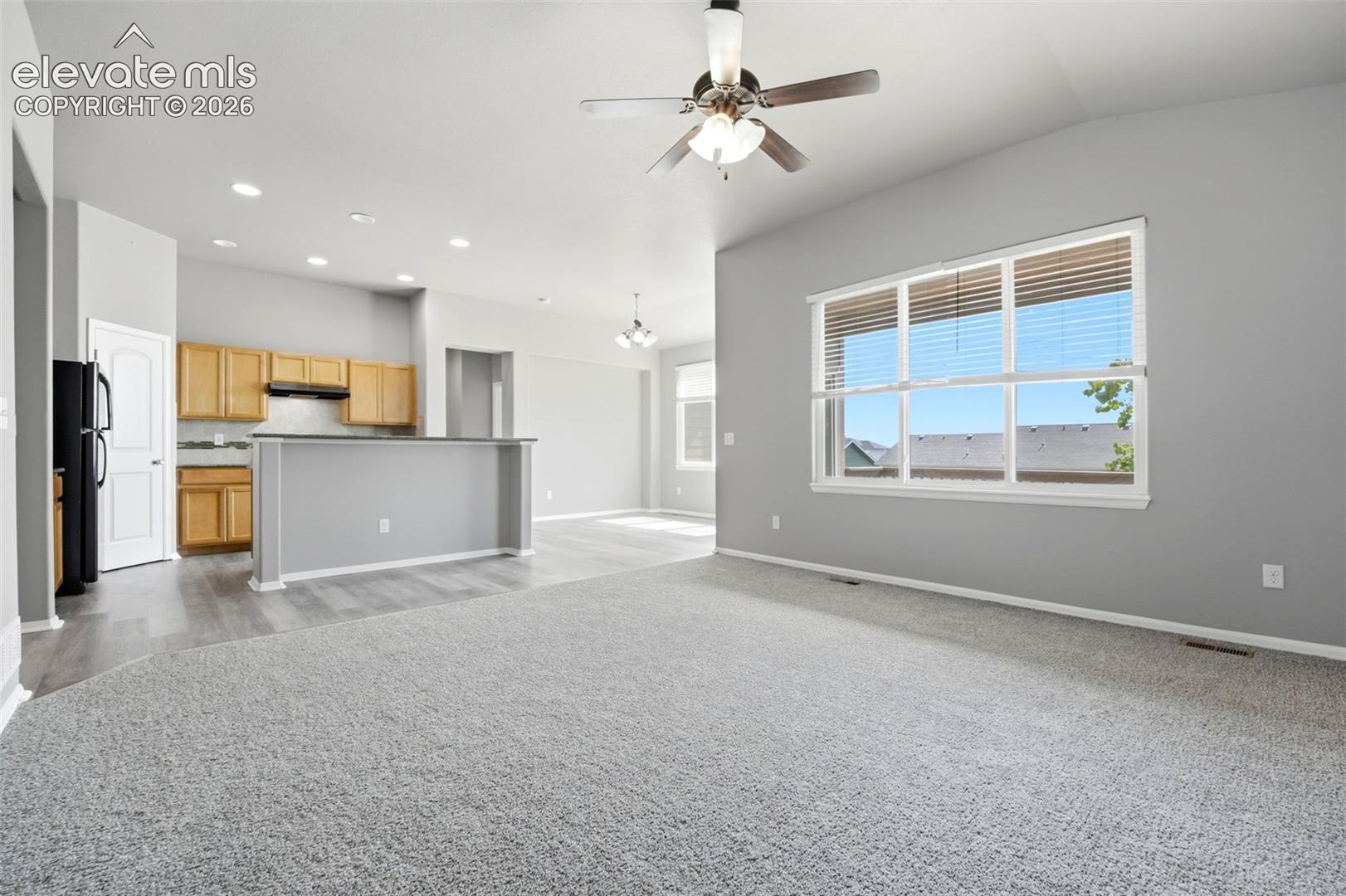 Vaulted ceilings, a ceiling fan with light fixture, large window, wood-finish flooring, and light-toned cabinetry