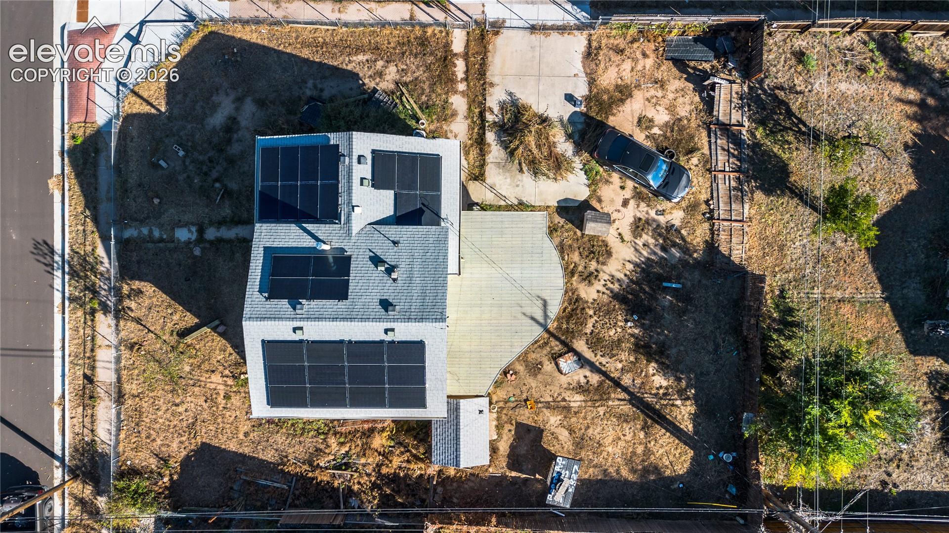 Aerial perspective of the property featuring a roof-mounted solar array, a concrete patio, and a concrete driveway
