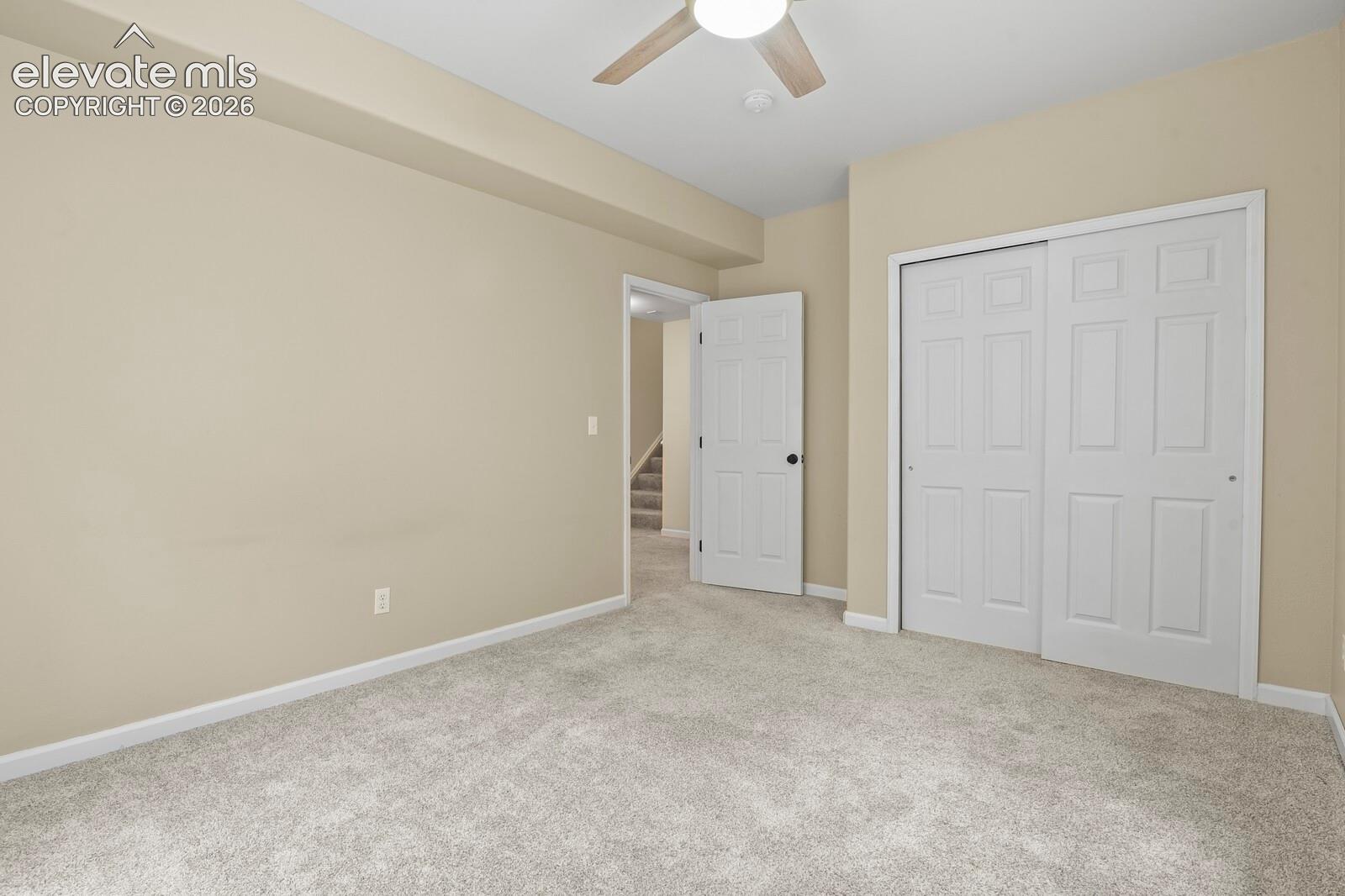 Carpeted room with a ceiling fan, light beige walls, white baseboards, and a double sliding closet with white paneled doors