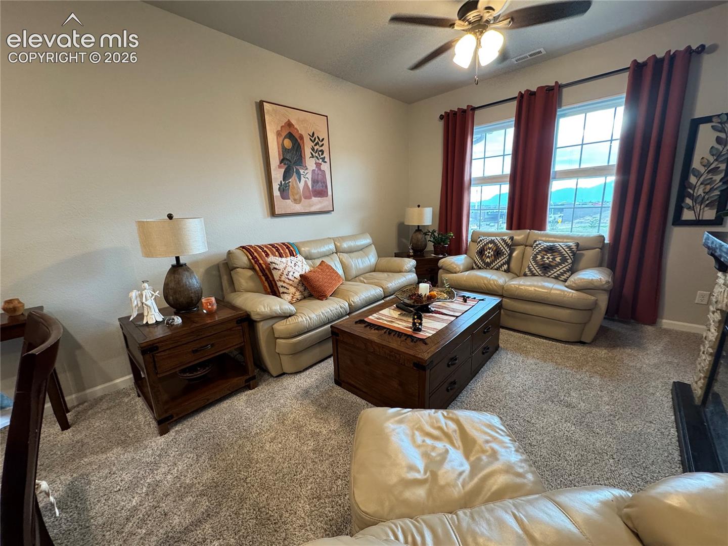 Living space featuring neutral carpeting, a ceiling fan, and large windows with natural light