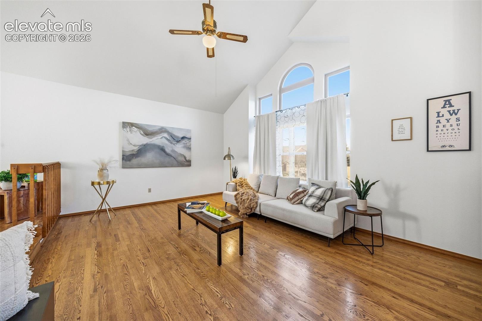 Vaulted ceilings, wood-finish flooring, and arched windows with multi-pane glass, complemented by a ceiling fan