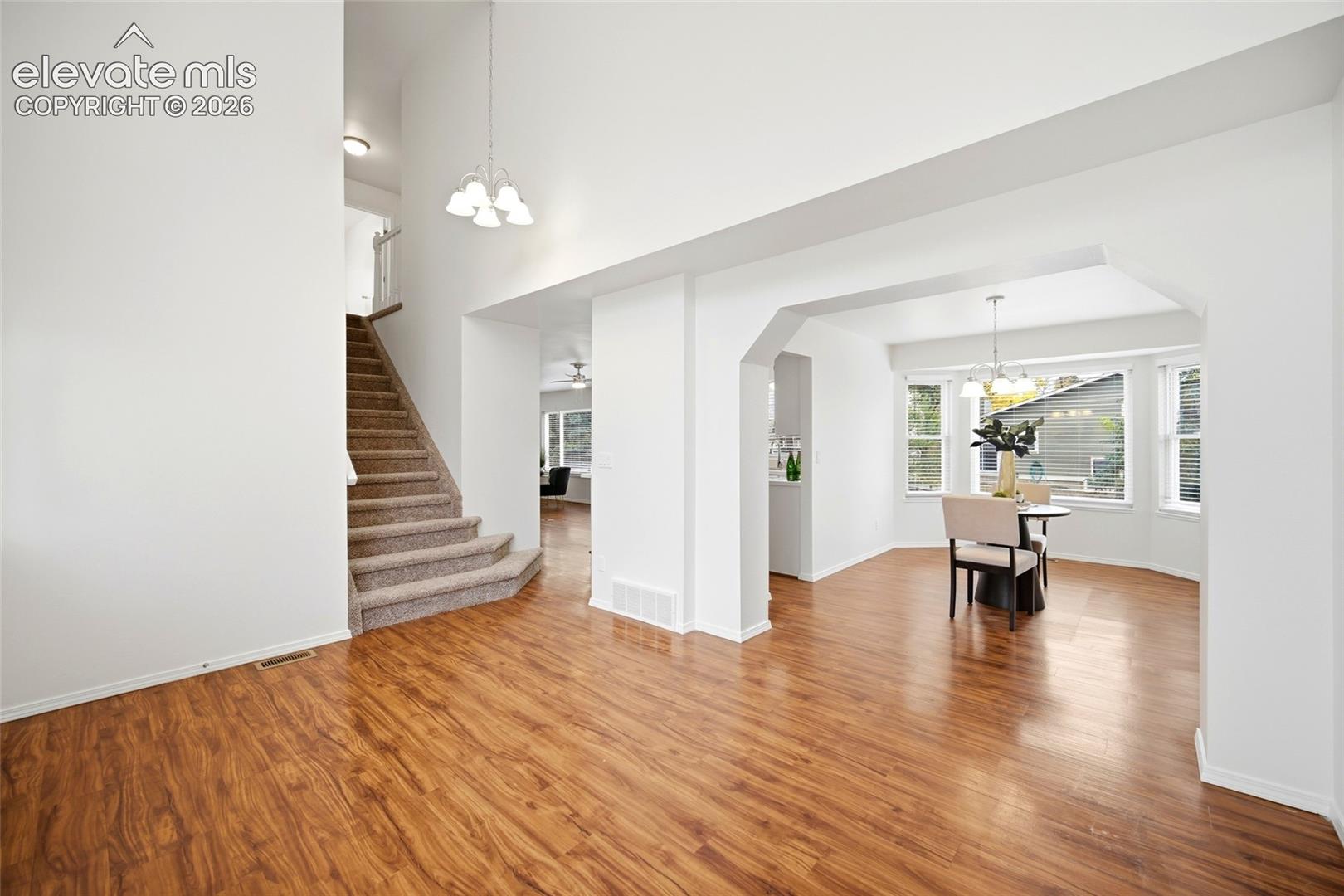 Vaulted ceilings, wood-finish flooring, staircase with neutral carpeted treads, and multiple windows providing natural light