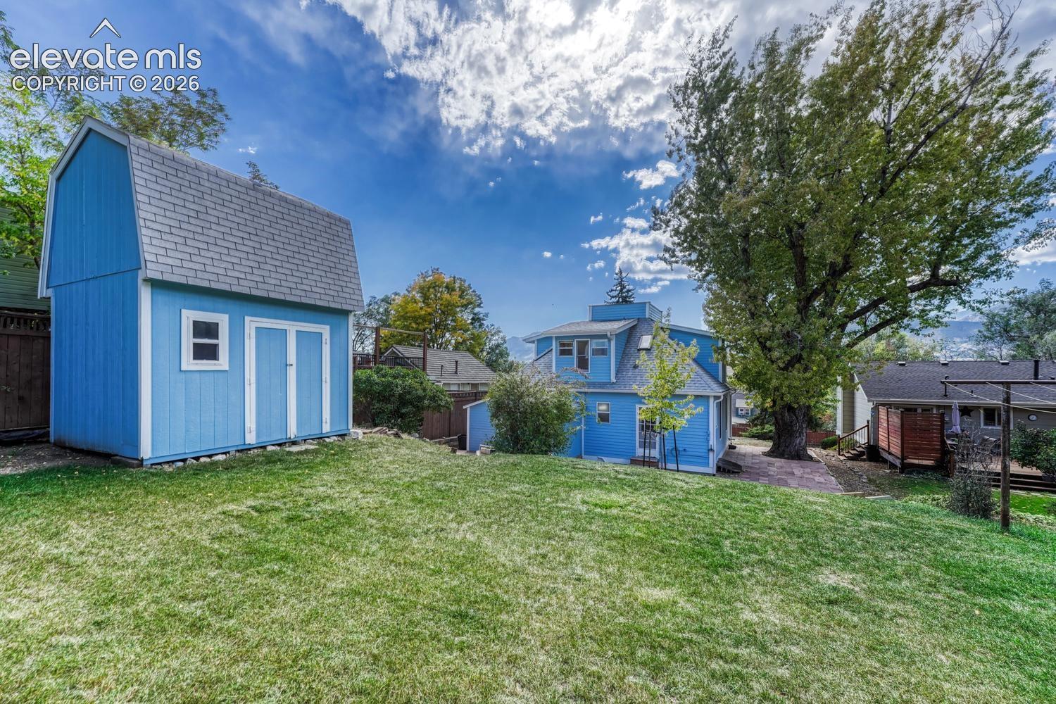 Expansive grassy yard with a detached storage shed, mature trees, and flagstone paving