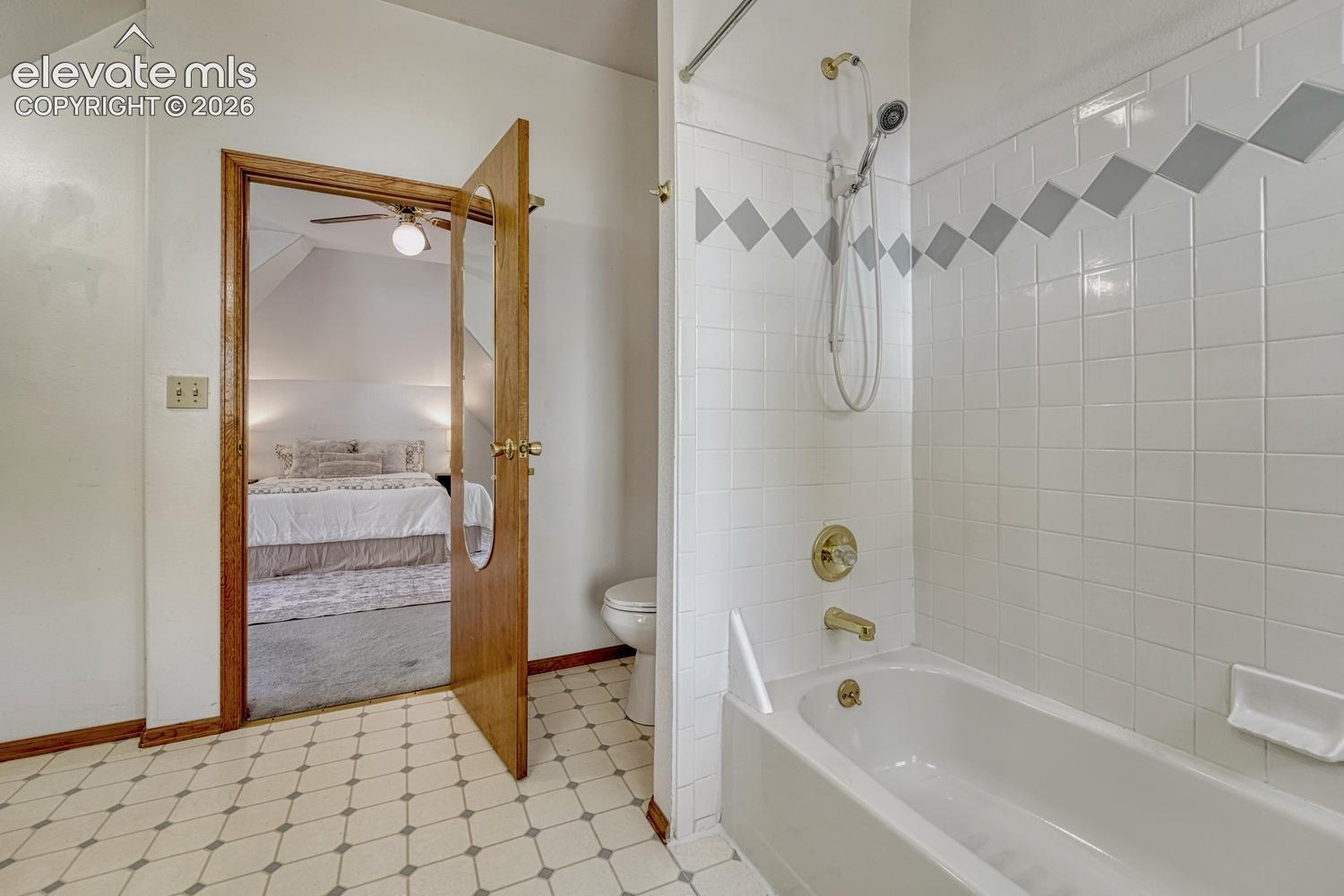 Bathtub and shower combination with white subway tile and decorative accent band, featuring brass fixtures