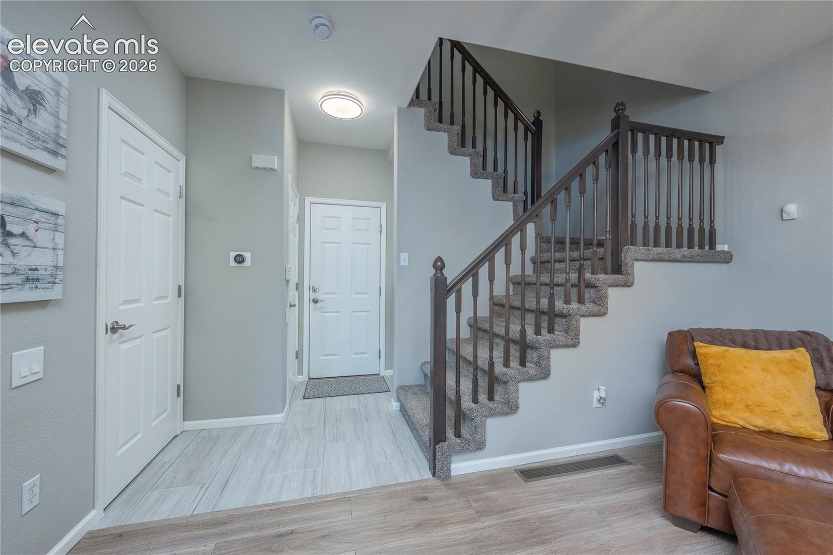 Entryway featuring light-toned tile flooring, wood-finish flooring, a six-panel door, and a staircase with stained wood handrails and carpeted treads