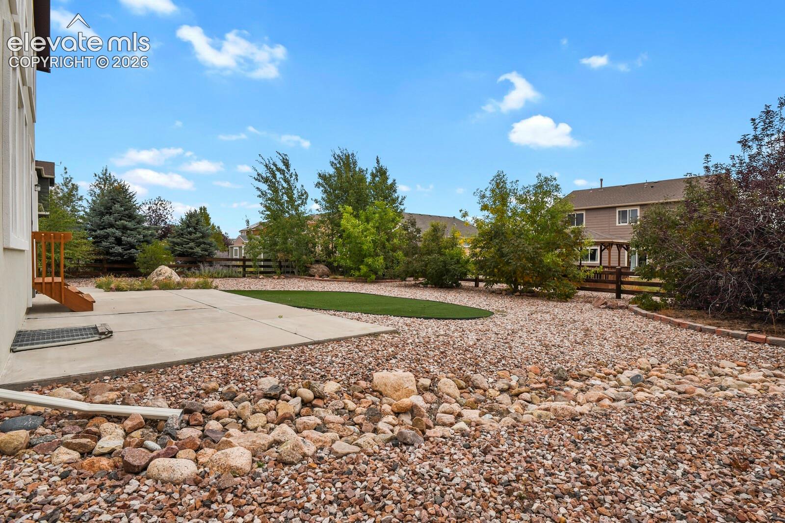 Expansive backyard featuring a concrete patio, artificial turf area, decorative rock landscaping, and a wood fence