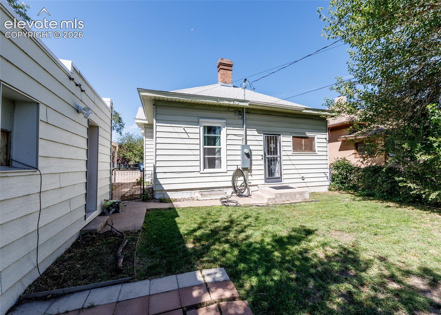 Rear exterior with horizontal siding, brick chimney, and a concrete patio