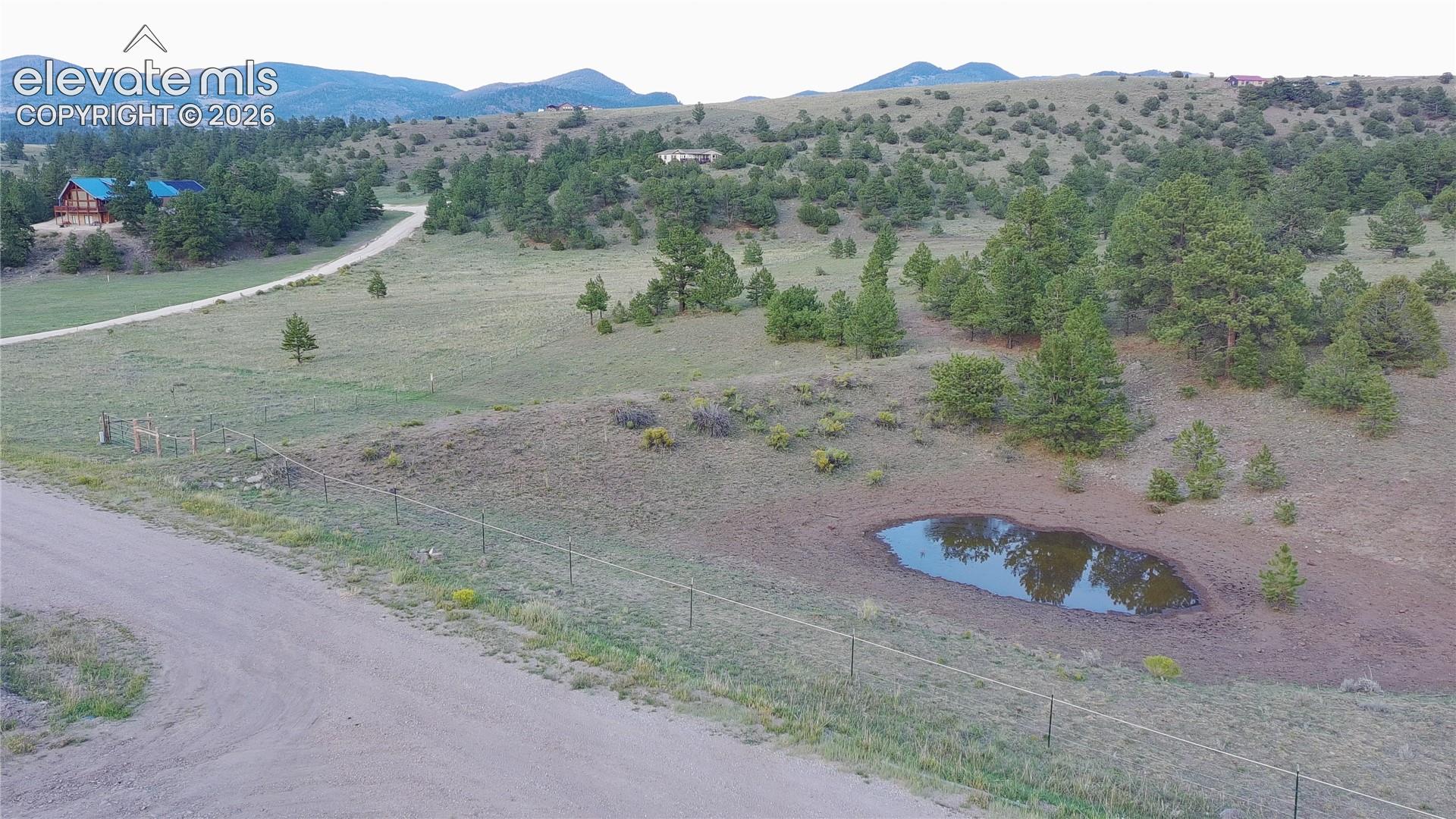 Expansive rural acreage featuring rolling pastureland with scattered mature trees, fencing, and a natural pond