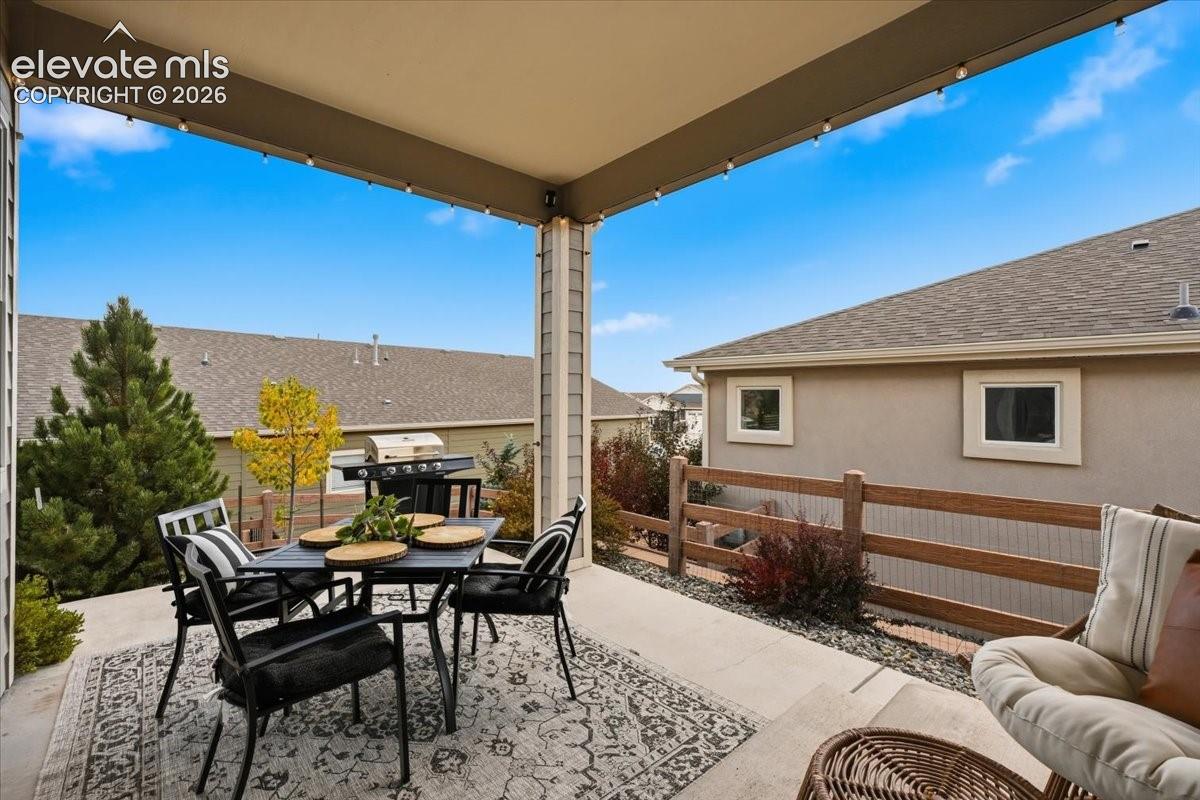 Covered patio with string lighting, concrete flooring, and wooden fencing
