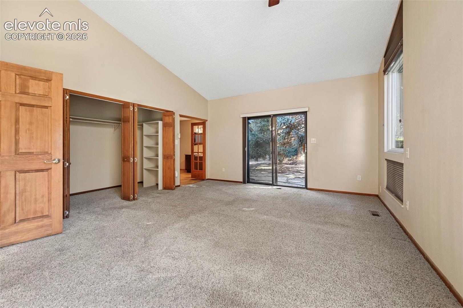 Vaulted ceiling, sliding glass door, built-in closet shelving, and natural wood doors