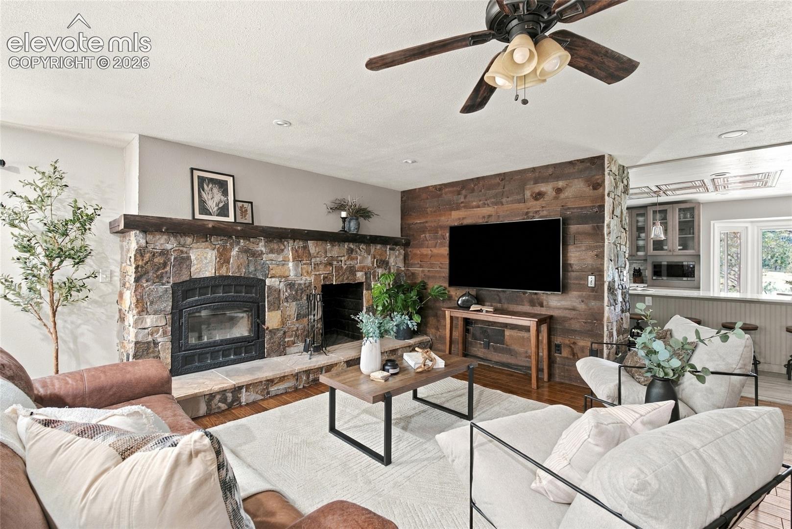 Stone fireplace with wood mantel, wood-finish flooring, wood plank accent wall, recessed lighting, and a ceiling fan with light fixture