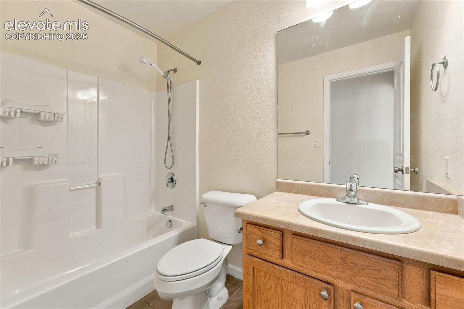 Bathroom featuring a shower and tub combination with a molded surround, wood-finish cabinetry, a neutral-toned countertop with an integrated oval sink, and a large wall-mounted mirror