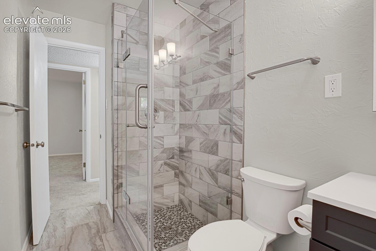 Spa-inspired primary bathroom featuring a frameless glass walk-in shower with marble-look tile surround and pebble floor accent, white porcelain toilet, floating vanity with integrated sink, chrome fixtures, and neutral tile flooring throughout