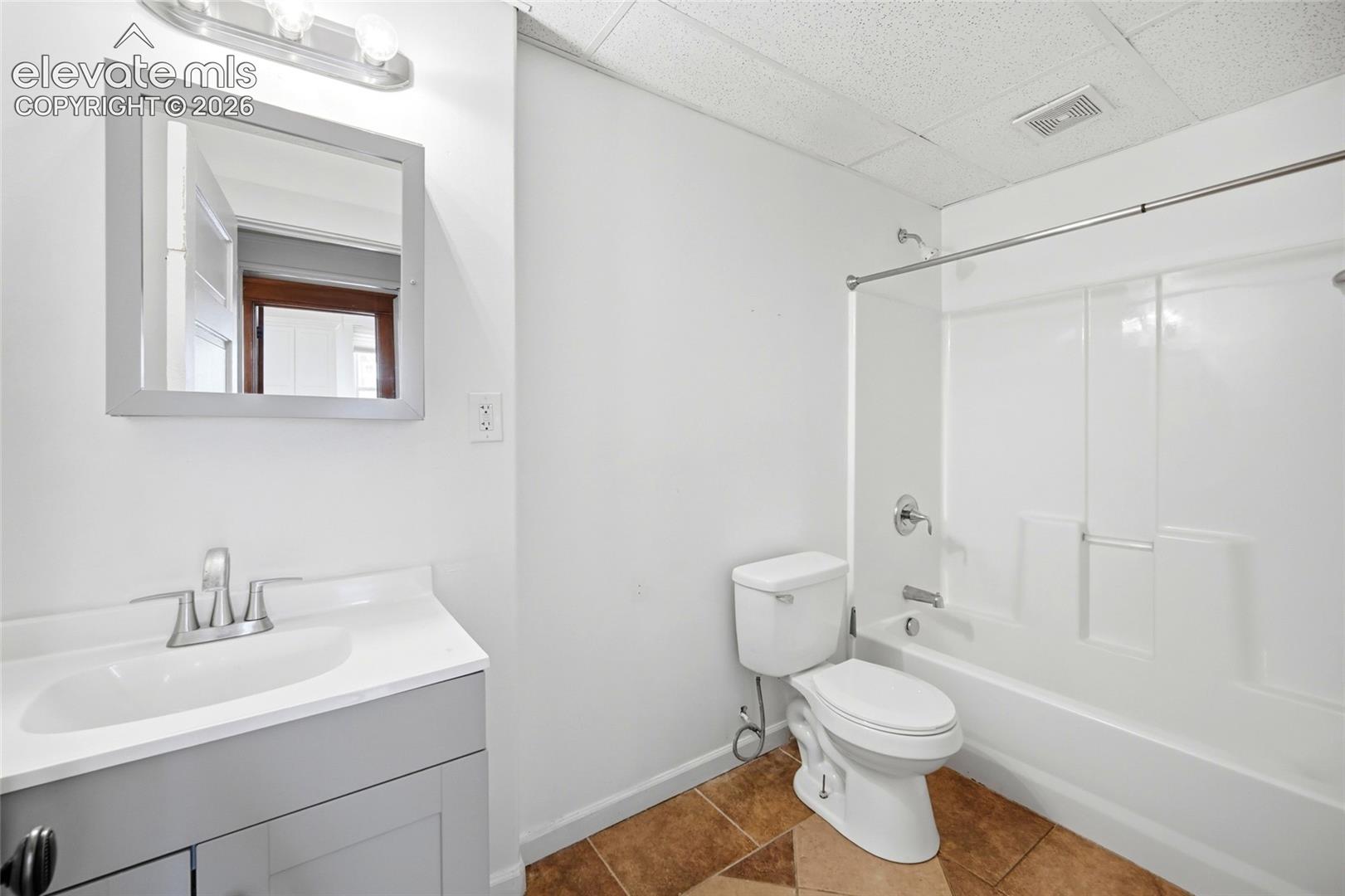 Bathroom featuring a vanity with a white composite countertop and integrated basin, a framed wall mirror, polished chrome dual-handle faucet, tile-patterned flooring, and a tub-shower combination with an integrated surround