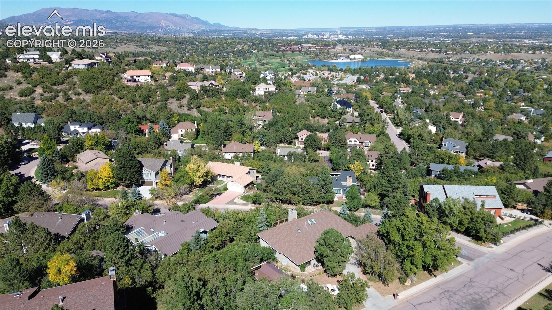 Aerial perspective of the residential landscape featuring dense mature trees, varied architectural styles, asphalt streets, and a mountainous horizon