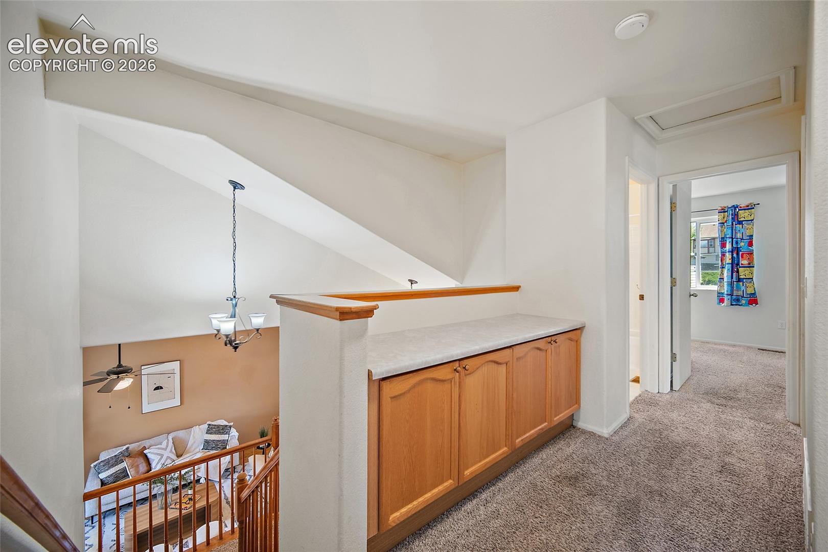 Upper-level hallway featuring a built-in wood-finish cabinet with a light-toned countertop, carpet flooring, and a railing overlooking the lower level