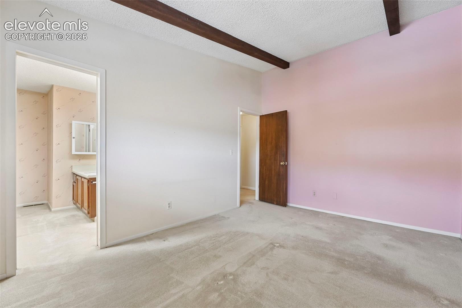 Vaulted ceilings with exposed wood beams, carpeted flooring, and an en-suite bathroom with a wood vanity
