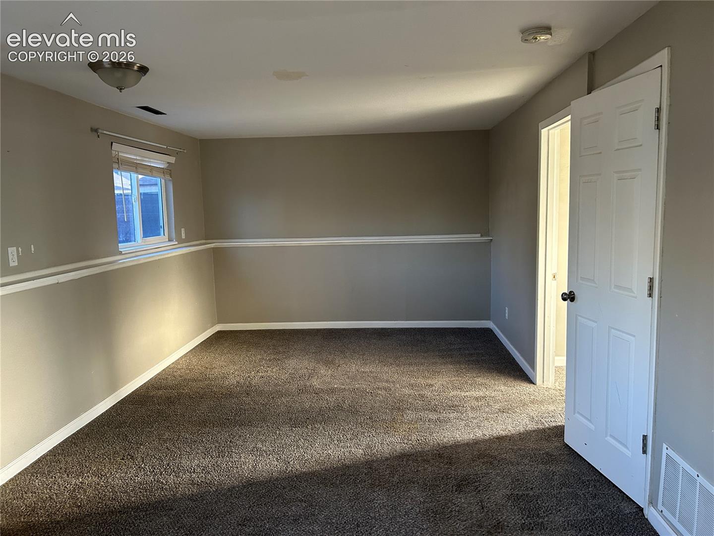 Interior room featuring wall-to-wall carpeting, neutral-toned walls, decorative chair rail molding, and a white paneled door