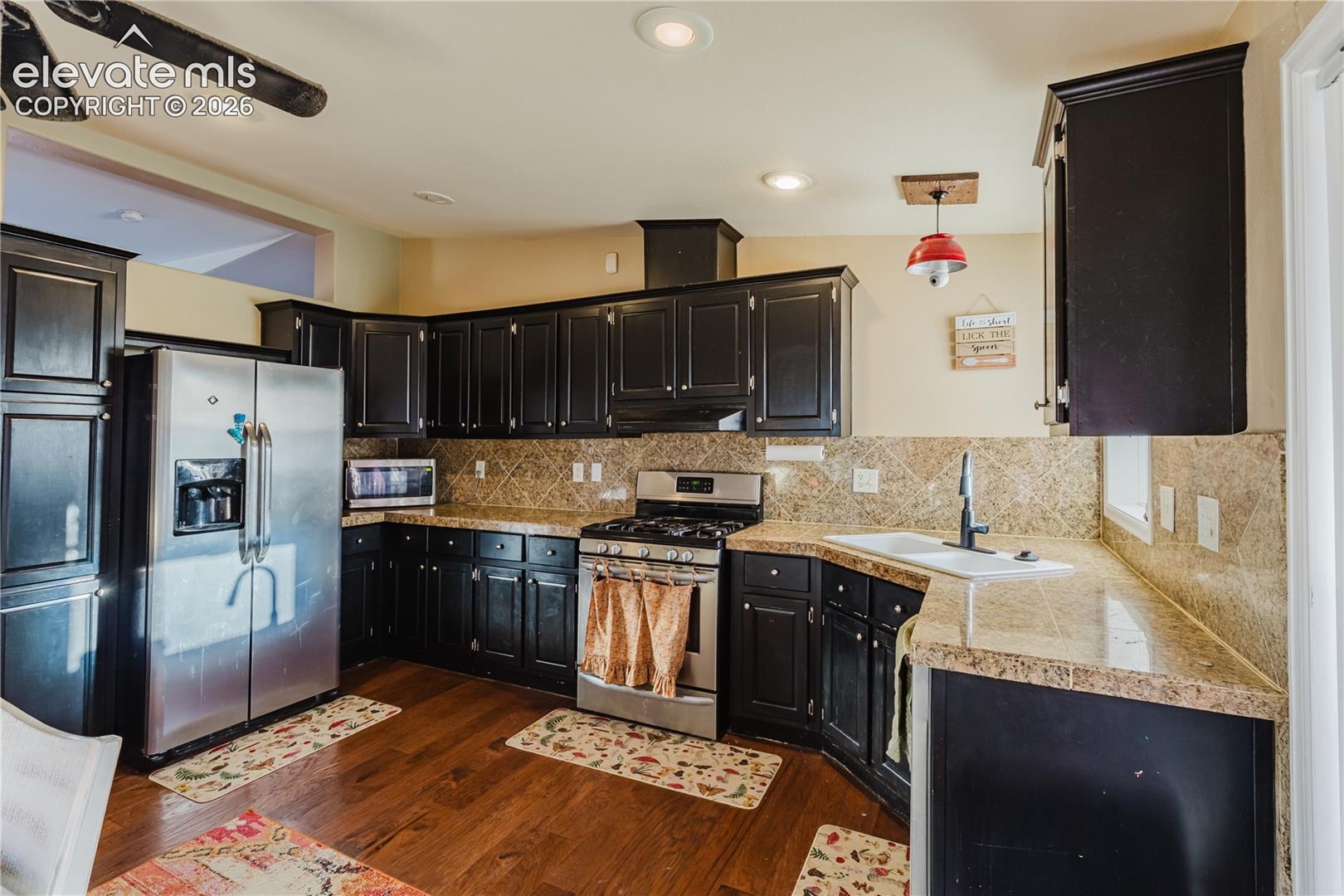 Kitchen featuring dark wood cabinetry, stainless steel appliances, light-toned countertops, tile backsplash, and wood-finish flooring