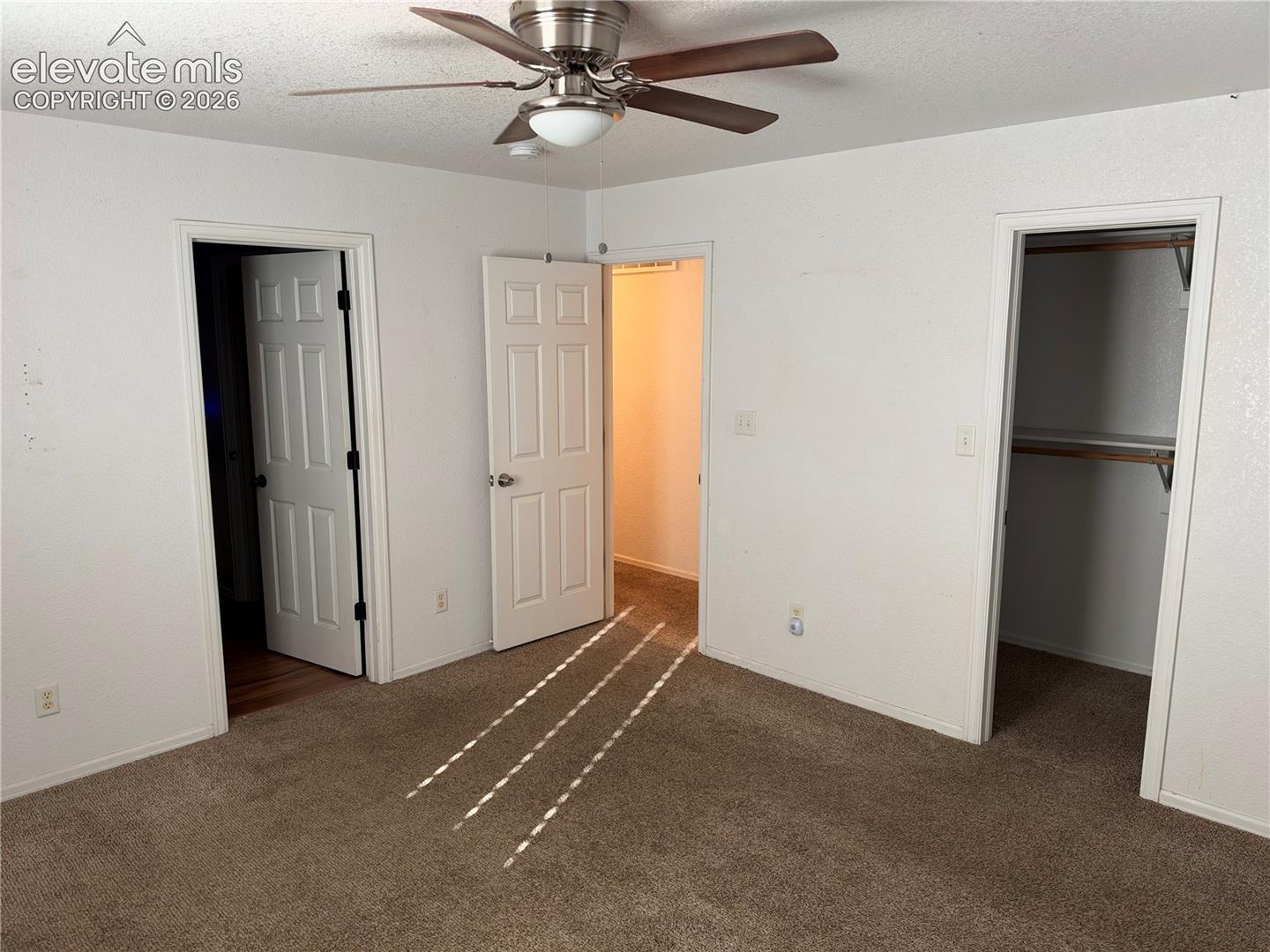 Room featuring neutral wall-to-wall carpeting, a ceiling fan with integrated lighting, and multiple interior doors providing access to closet and hallway spaces