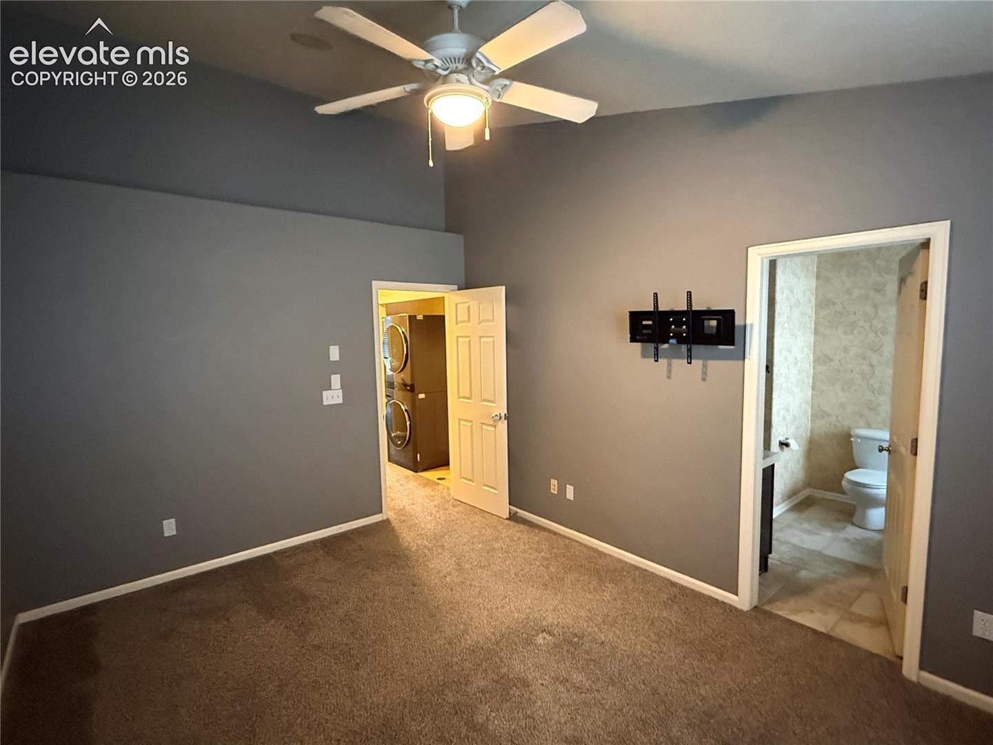 Vaulted ceiling featuring a central five-blade lighted ceiling fan, neutral wall finishes, and wall-mounted television bracket