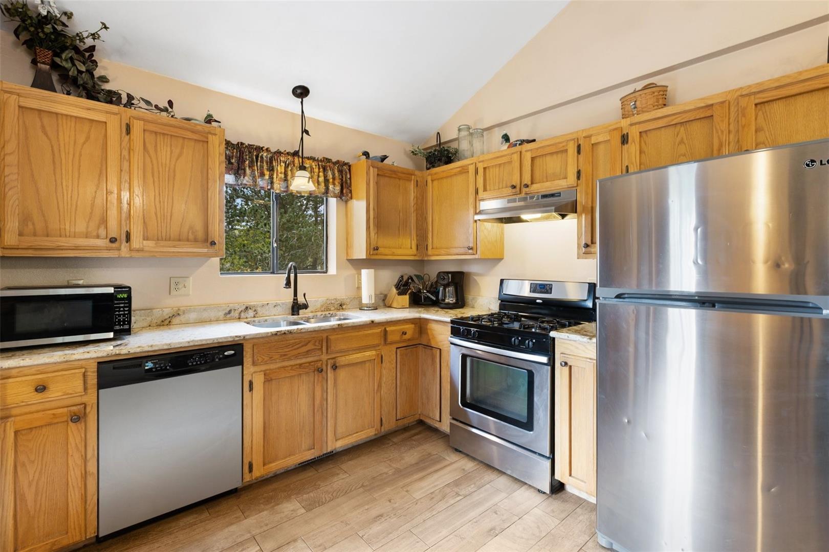 Kitchen featuring wood-finish cabinetry, stainless steel appliances, granite-style countertops, and wood-finish flooring