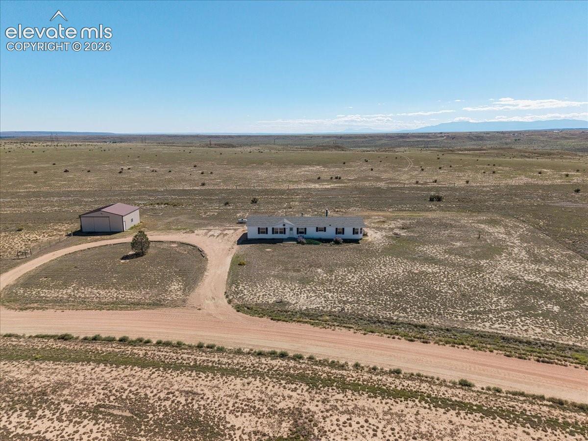 Expansive property featuring a single-story residence with a detached metal building, a circular drive, and a dirt road entrance