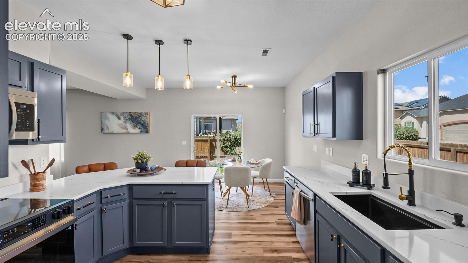 Kitchen featuring dark blue cabinetry, white countertops, stainless steel appliances, wood-finish flooring, and pendant lighting