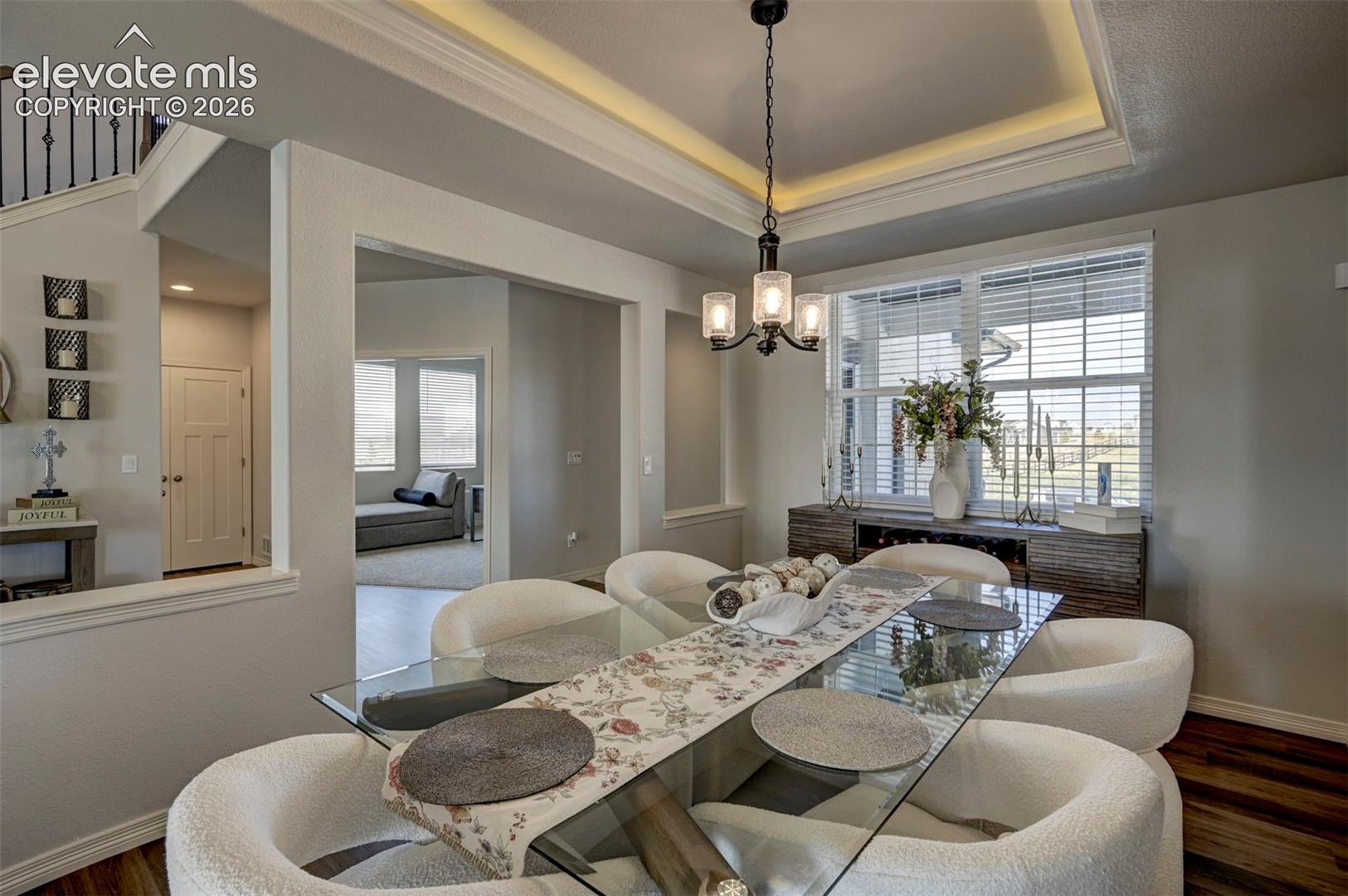 Dining area featuring a glass-top table, a contemporary chandelier, and tray ceiling with perimeter lighting