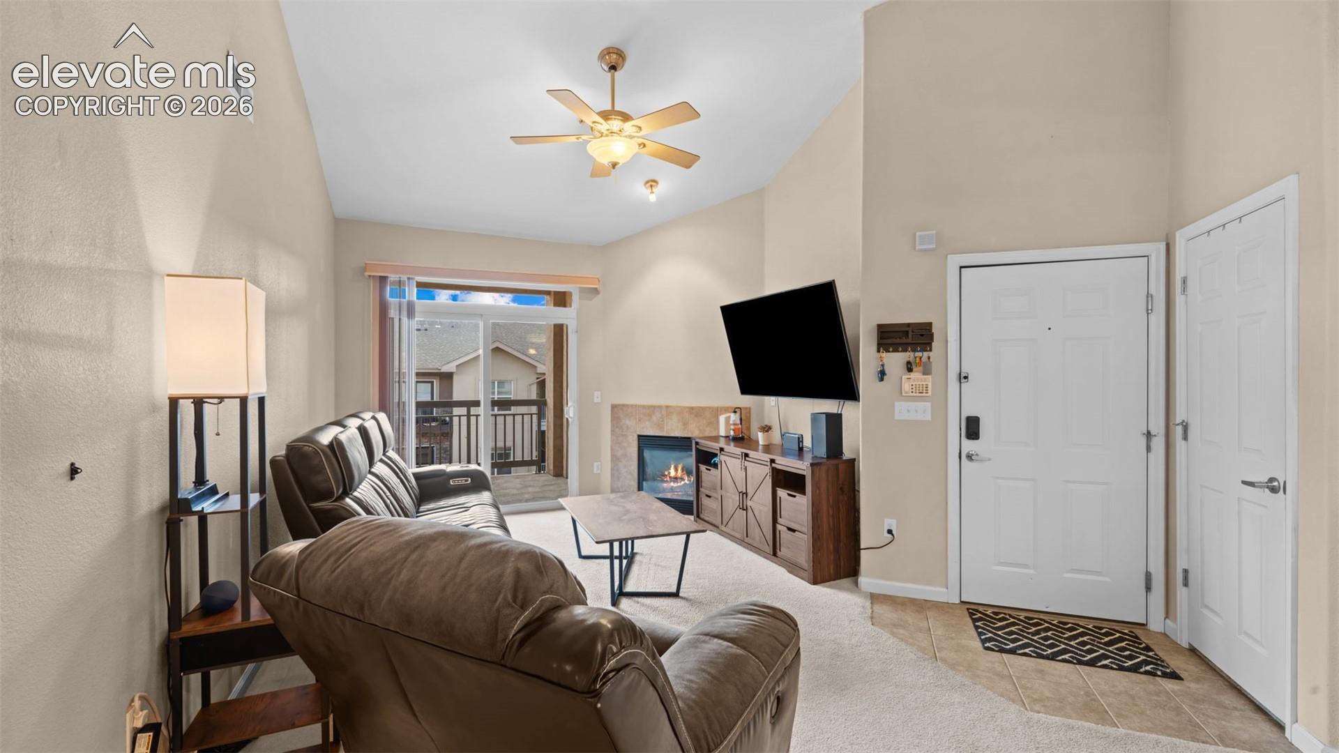 Vaulted ceiling living space featuring a ceiling fan with integrated lighting, a gas fireplace with a stone surround, and a sliding glass door to an outdoor deck