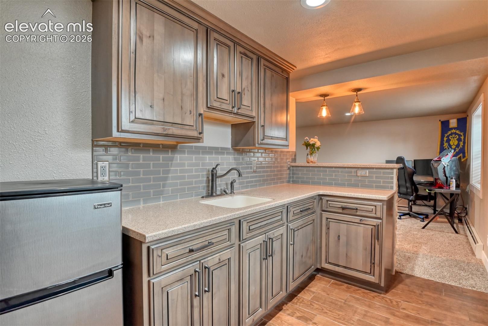 Kitchen featuring stainless steel refrigerator, tasteful backsplash, light wood-style floors, an office area, and a textured wall