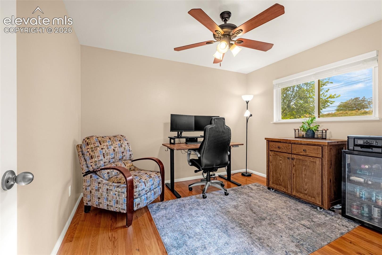Secondary bedroom on the main level with hardwood flooring, a window providing natural light, and a ceiling fan with integrated lighting
