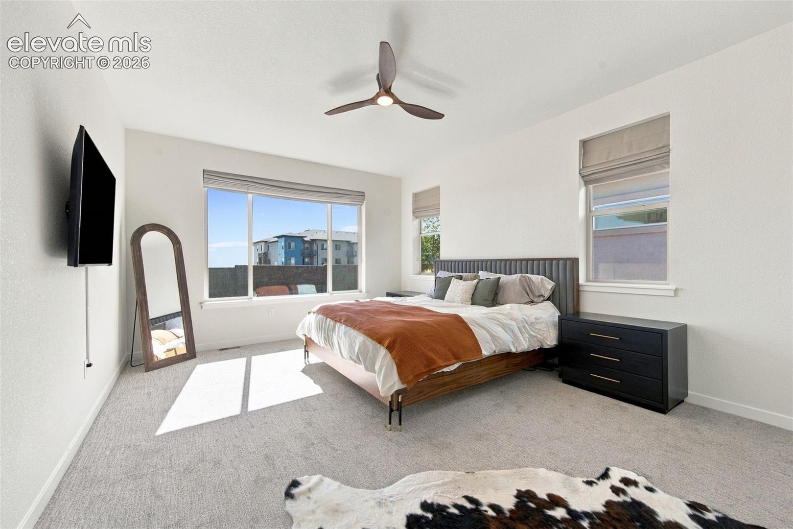 Interior space featuring neutral-toned carpeting, three large windows with roller shades, and a ceiling-mounted fan with integrated lighting