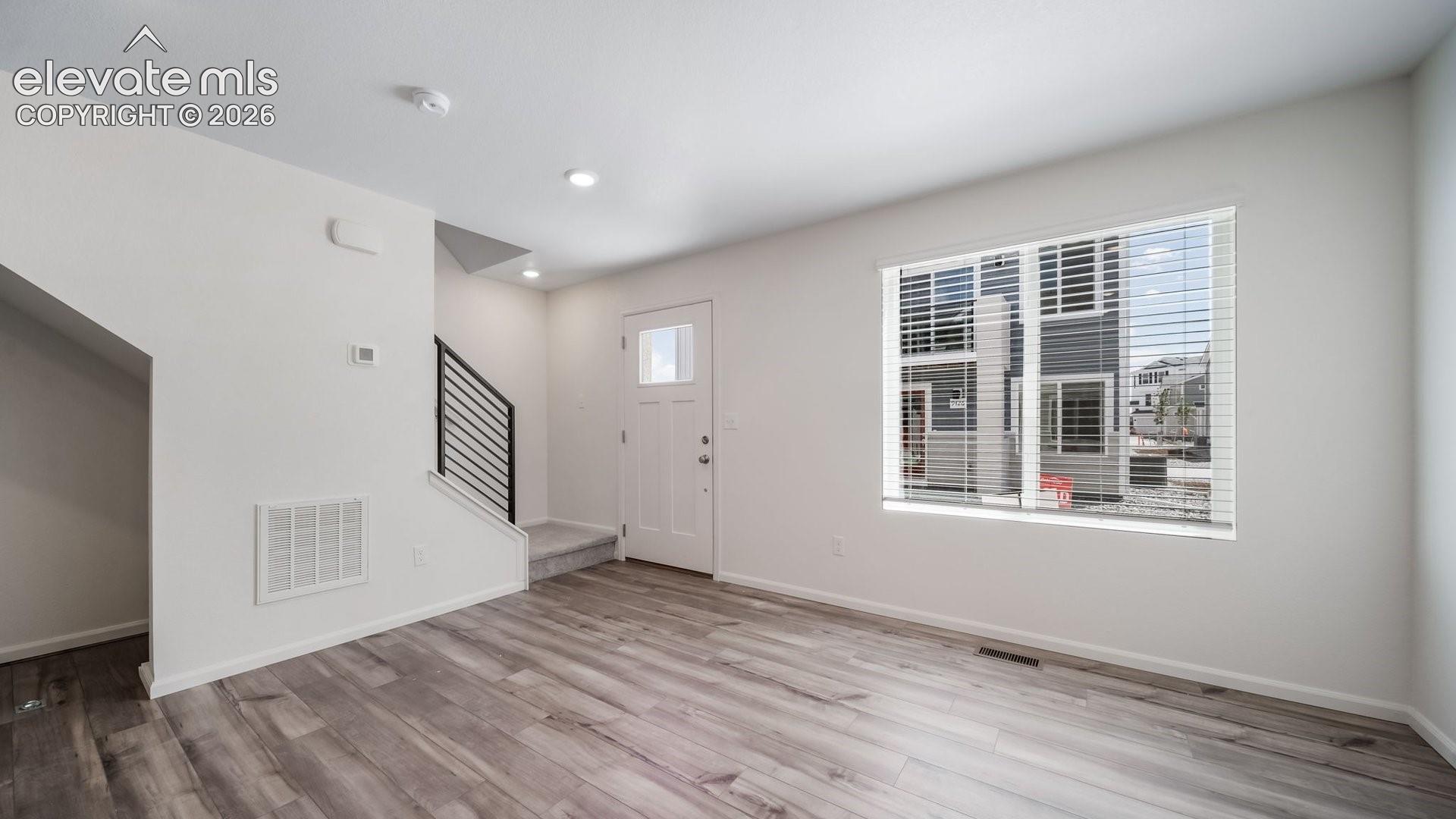 Neutral interior space featuring wood-finish flooring, recessed lighting, and a metal horizontal-bar staircase railing
*photos of a model home*