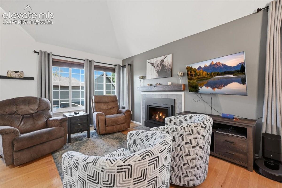 Living area featuring a vaulted ceiling, wood-finish flooring, multi-pane windows, and a fireplace with a tile surround and a wood mantel