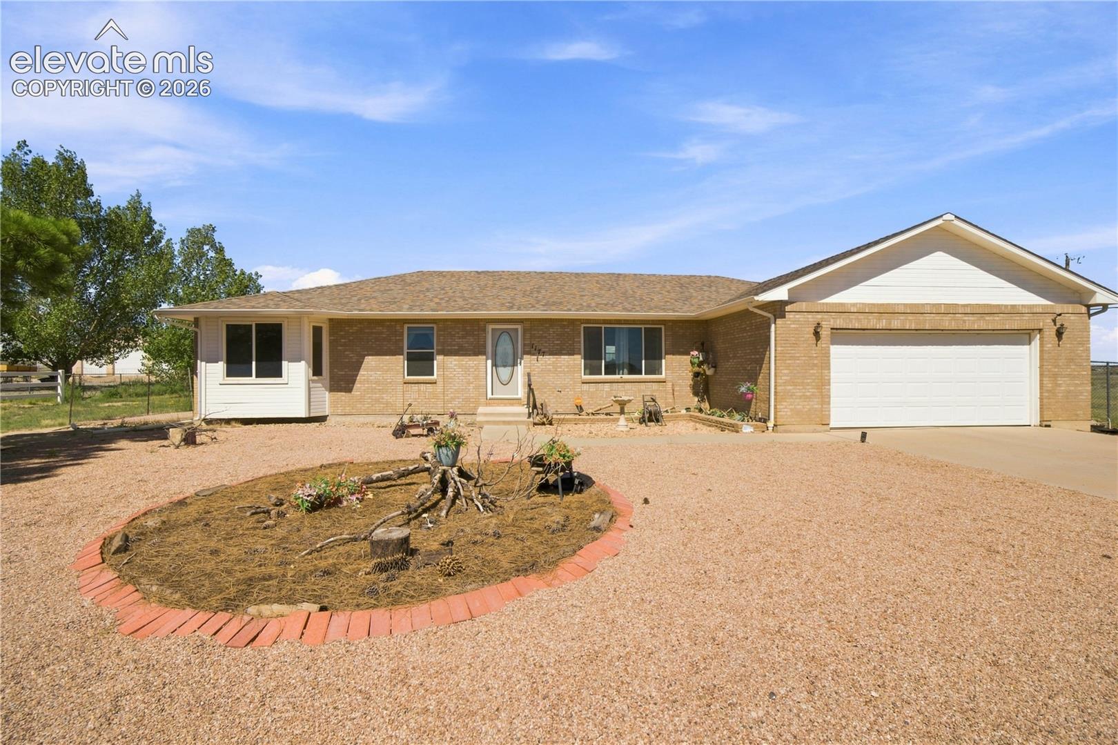 Brick exterior with a two-car garage, gravel driveway, and a bay window