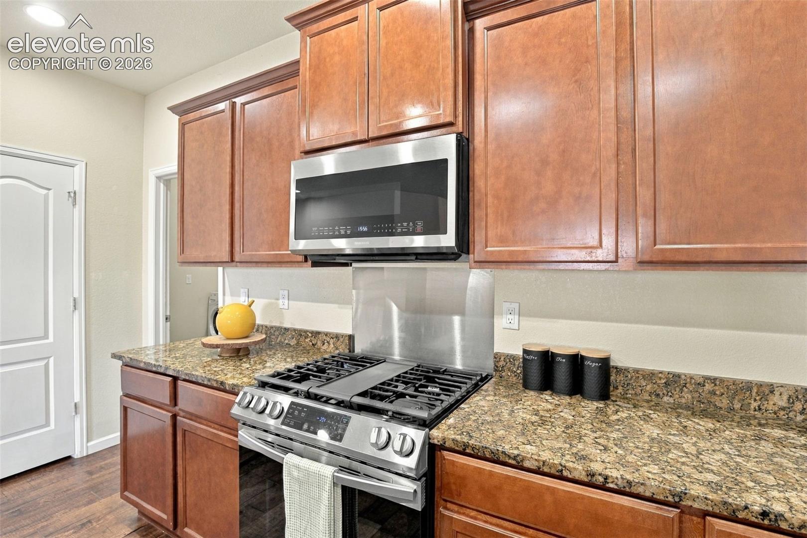 Kitchen featuring wood cabinetry, stone-surface countertops, a stainless steel gas range, and a mounted stainless steel microwave