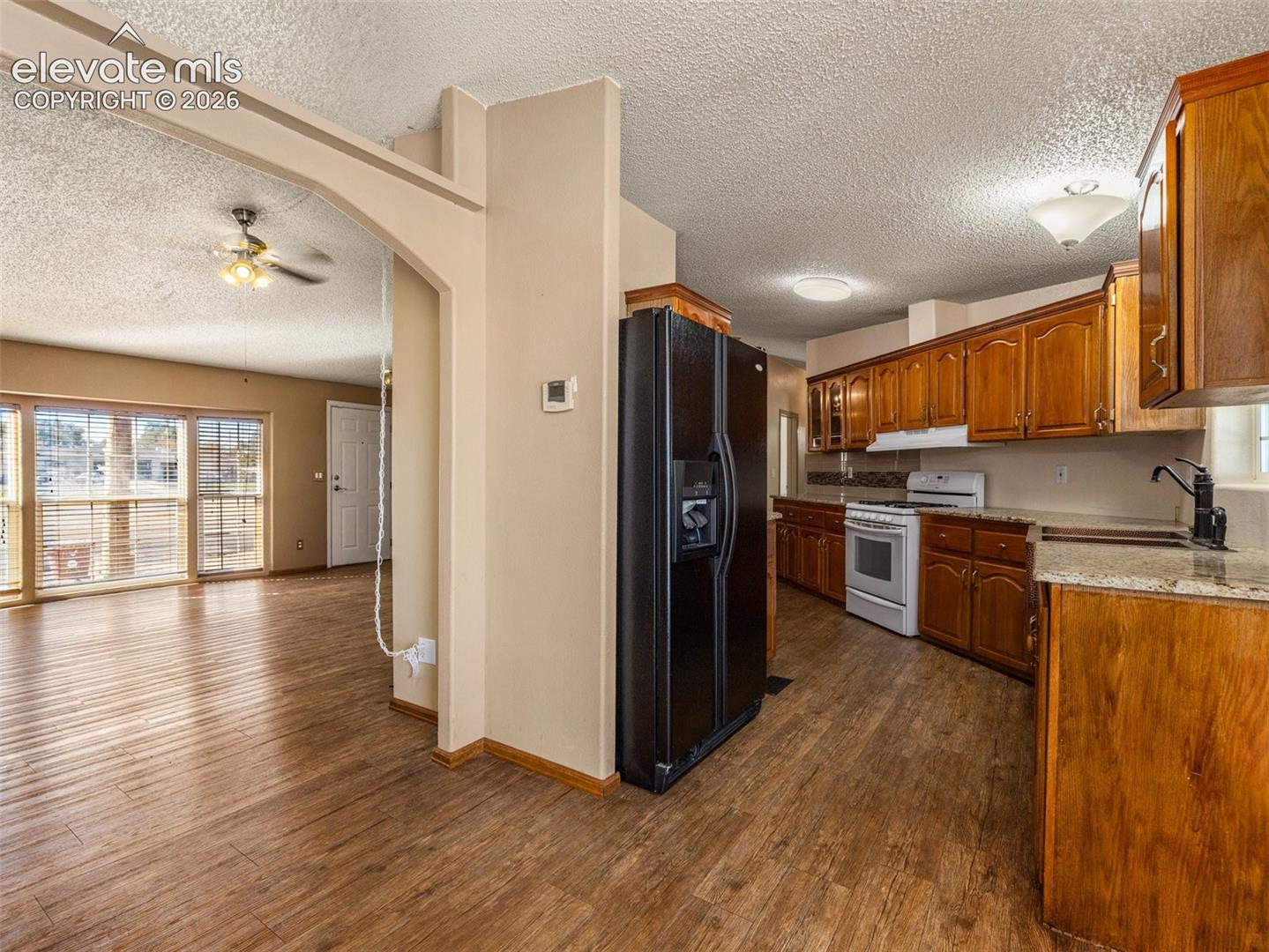 Kitchen featuring wood cabinetry, stone-finish countertops, built-in black refrigerator, white range, and wood-finish flooring