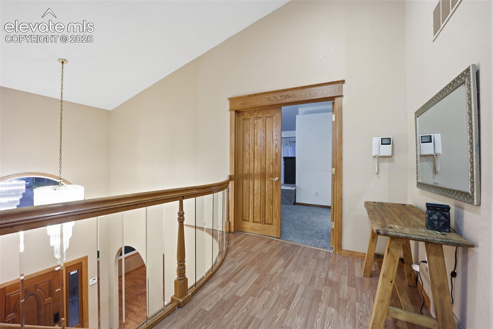 Wood-finish flooring, wood-paneled door, and a curved staircase with wood railing and clear balusters