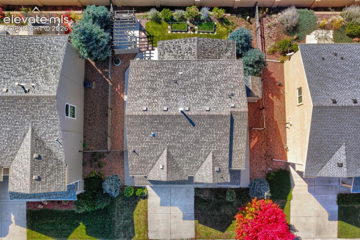 Aerial perspective featuring a multi-gabled composition shingle roof, a concrete driveway, a rear pergola, and perimeter fencing